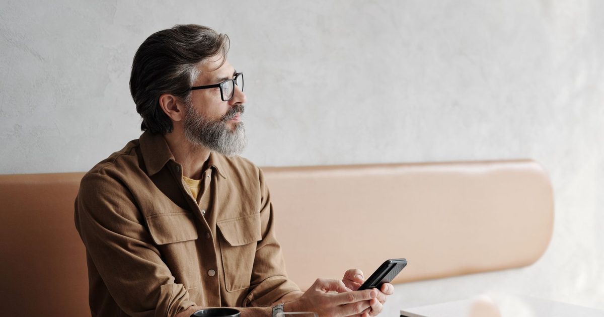 Homme barbu dans un café, téléphone en main, le regard pensif
