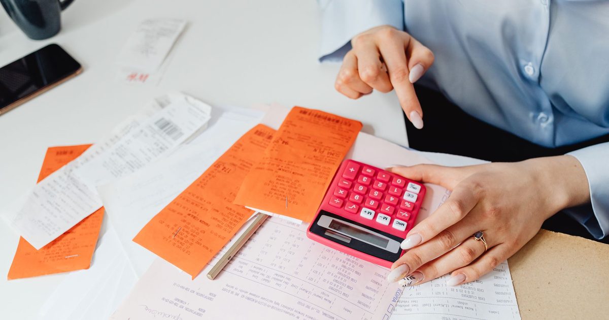 Mains avec calculatrice, reçus et chiffres manuscrits sur un bureau