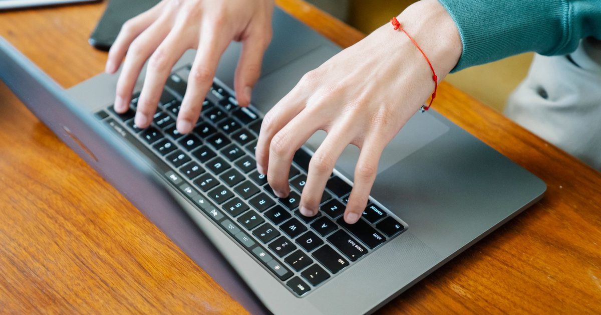 Mains tapant sur le clavier d’un ordinateur portable posé sur une table en bois