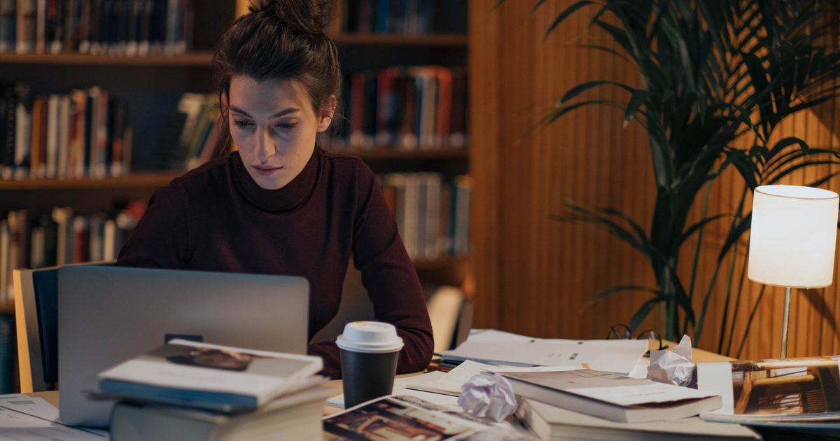 Femme travaillant à un bureau couvert de livres ouverts et d’un ordinateur portable